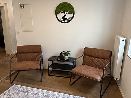 Modernes Sprechzimmer mit zwei braunen Sesseln, einem Tisch und Teppich in heller, minimalistischer Einrichtung.