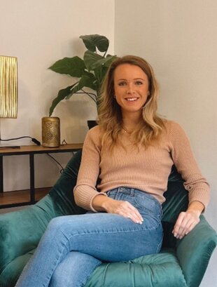 Psychotherapeutin Johanna Hartwig sitzt entspannt in einem grünen Sessel in modernem, gemütlichem Raum mit Regal, Lampe und Pflanze im Hintergrund.